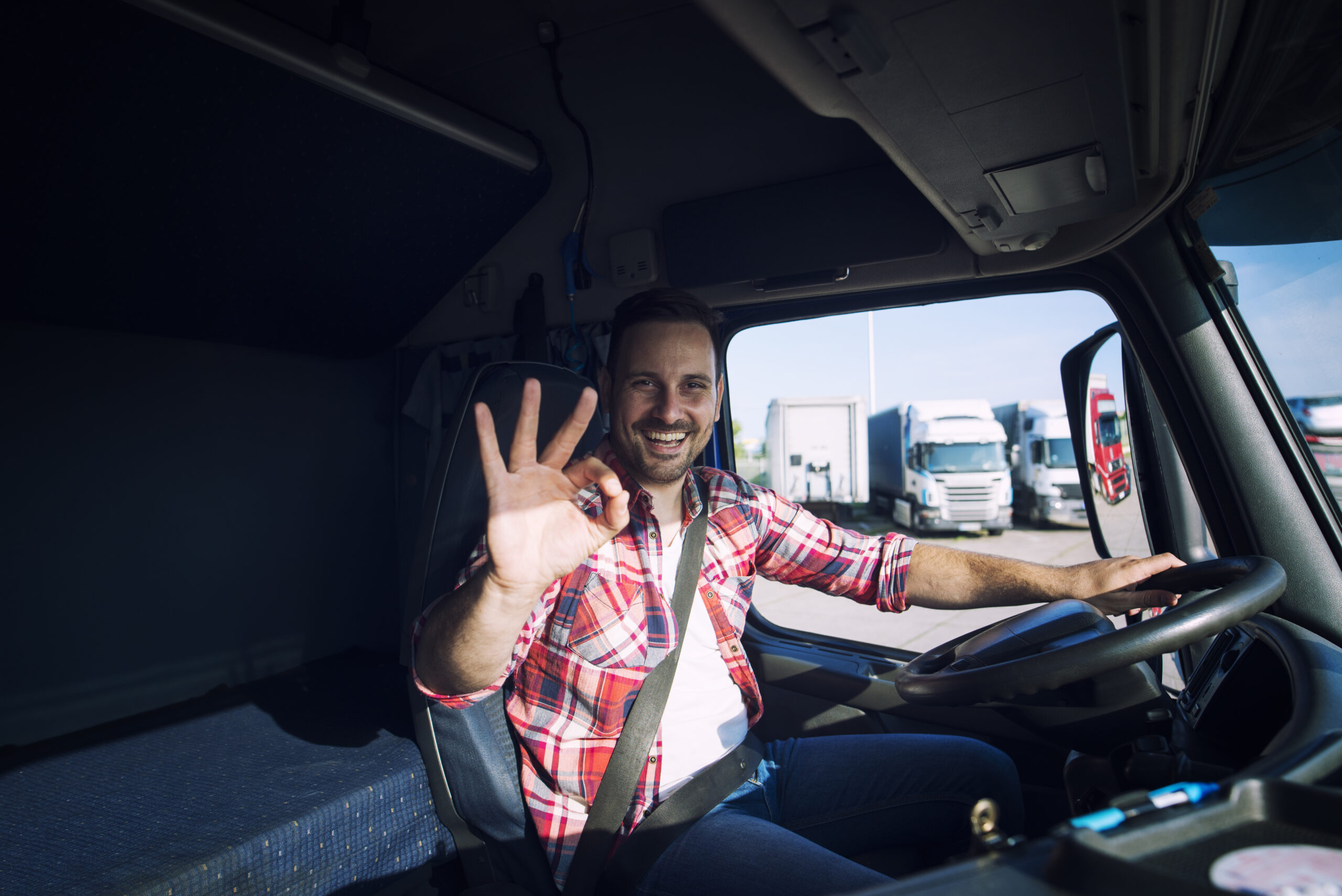 Truck driver loving his job and showing okay gesture sign while sitting in his truck cabin.